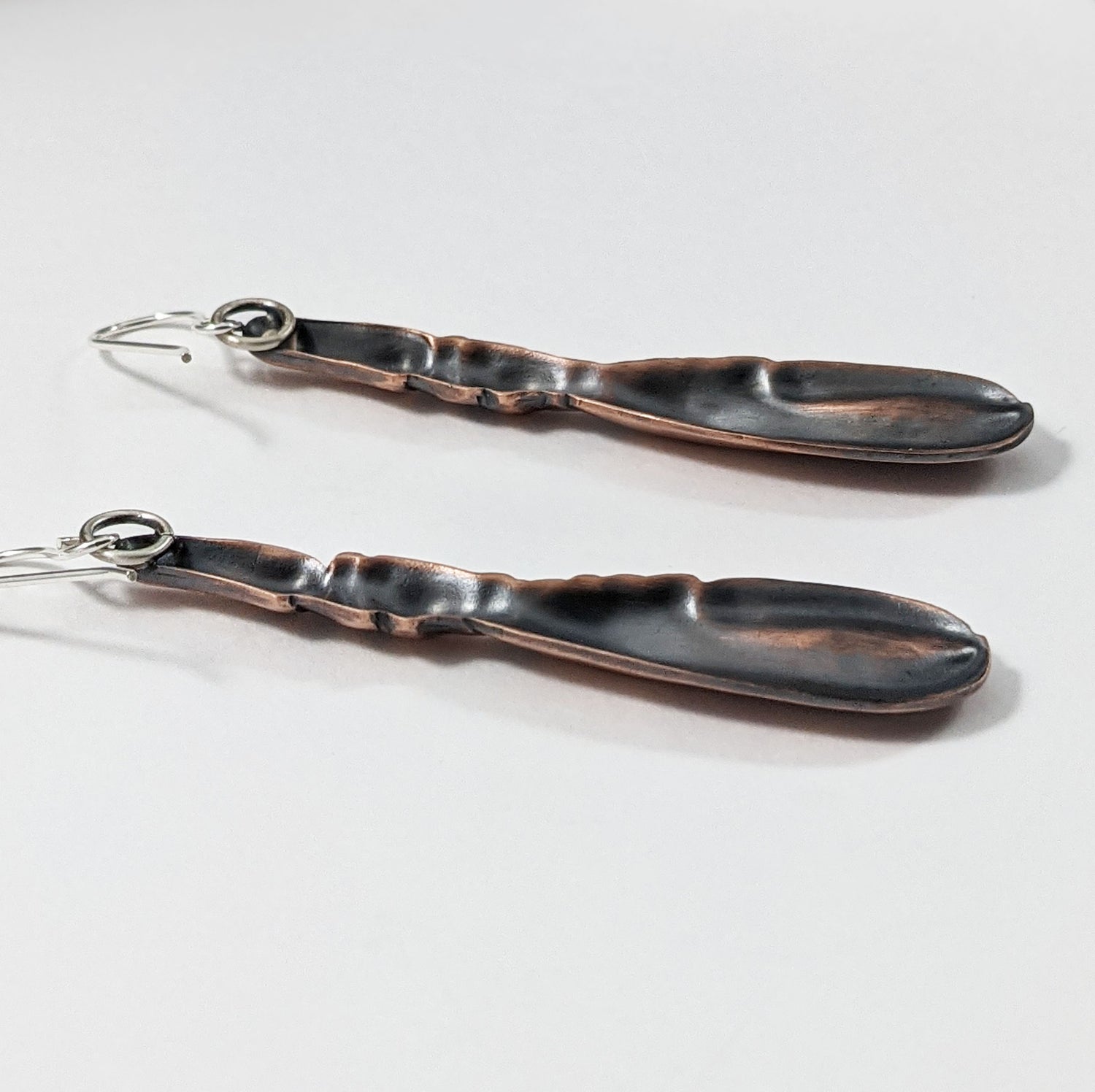 Copper earrings in the shape of a lobster claw. The claws are three dimensional and are on sterling silver ear wires. View of the back of the earrings showing that they are lightweight because they are hollow in the back.