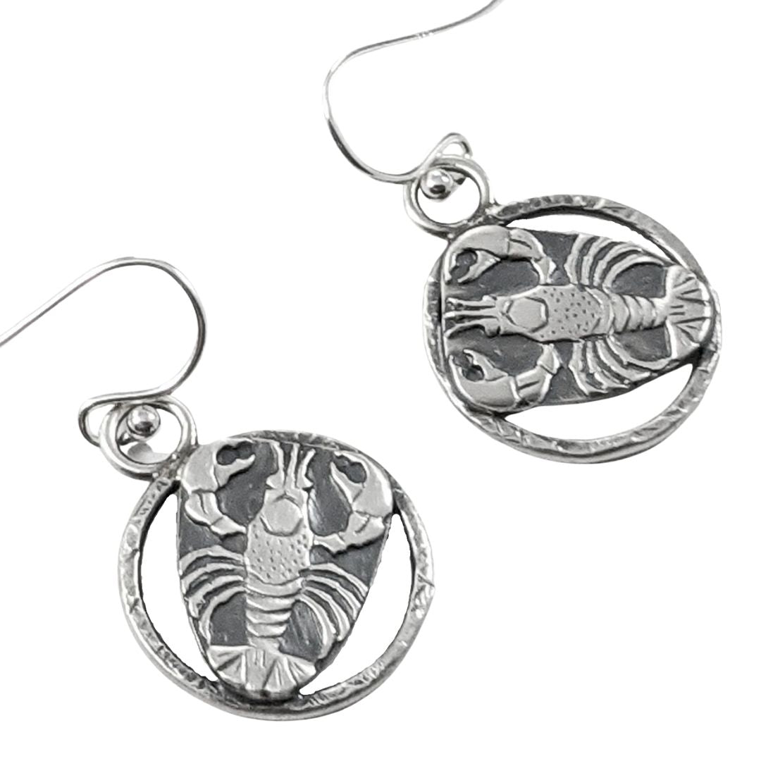 Sterling silver lobster earrings. The lobster is a detailed raised impression and is attached to a sterling open hoop that has a hammered texture design.