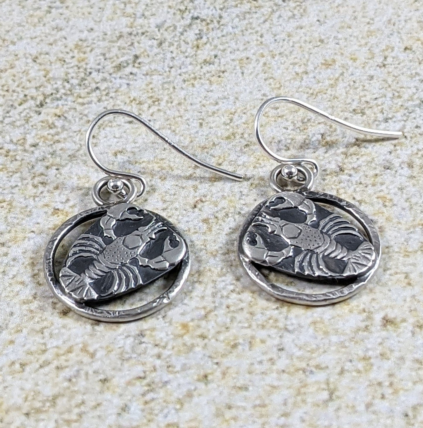 Sterling silver lobster earrings. The lobster is a detailed raised impression and is attached to a sterling open hoop that has a hammered texture design.