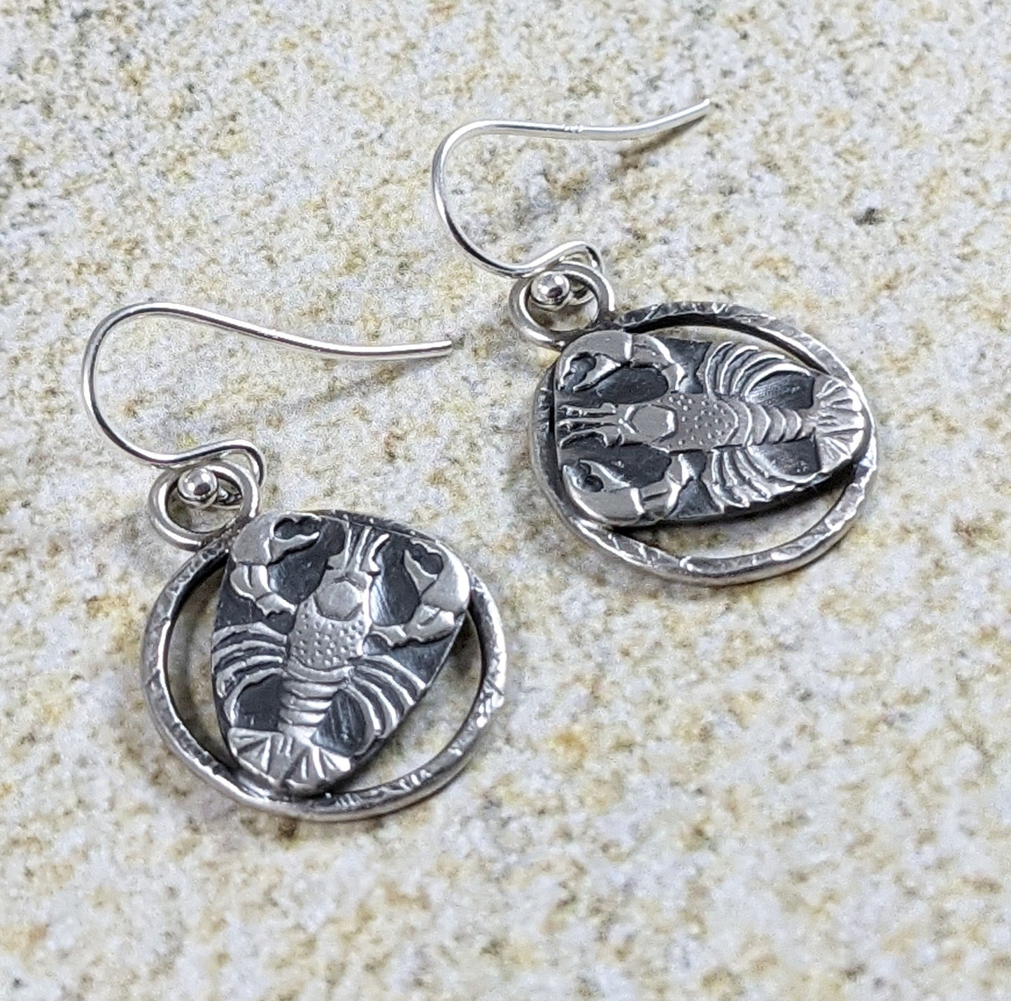 Sterling silver lobster earrings. The lobster is a detailed raised impression and is attached to a sterling open hoop that has a hammered texture design.