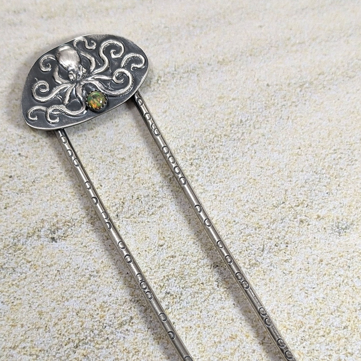 Octopus sterling silver hair fork. The octopus is a detailed raised design on a sterling silver sheet. There is a flashy 5mm opal below the octopus. The fork has stamped circles to represent octopus suckers.  fork and octopus design are blackened to show the details. The entire piece is handmade sterling silver.